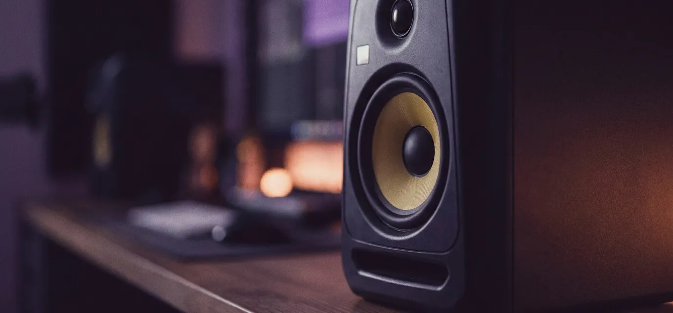 Studio monitor speaker on a desk with a DAW visible on screen in the background